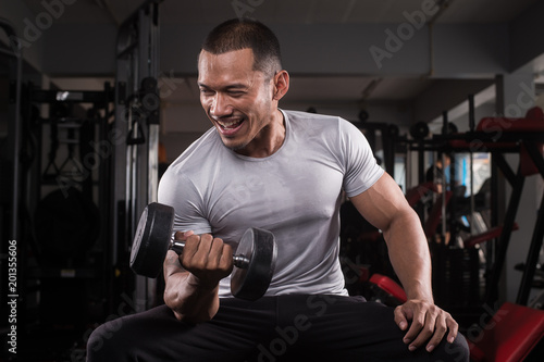 Muscular builder man training his body with dumbbell in Modern fitness center