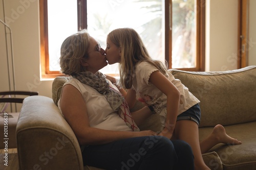 Mother and daughter kissing each other on sofa at home