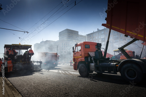 Asphalting construction works with commercial repair equipment road crews. Steam and smoke from hot bitumen at the steet under the sun and blue sky
