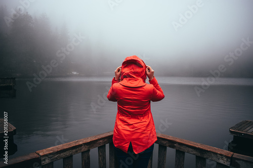 Rear view of young woman standing in front of waterfall with her hands raised. Female tourist with her arms outstretched looking at waterfall.