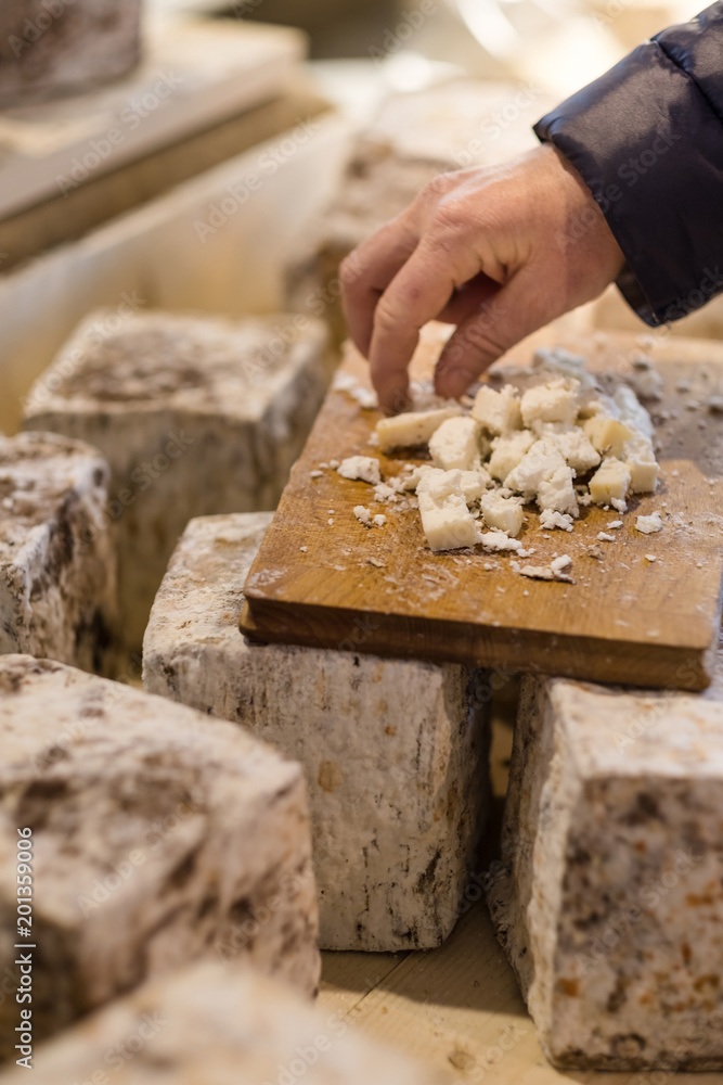 A cheesemonger is offering some cheese to try from large aged cheese loafs A cheesemonger is offering some cheese to try from large aged cheese loafs