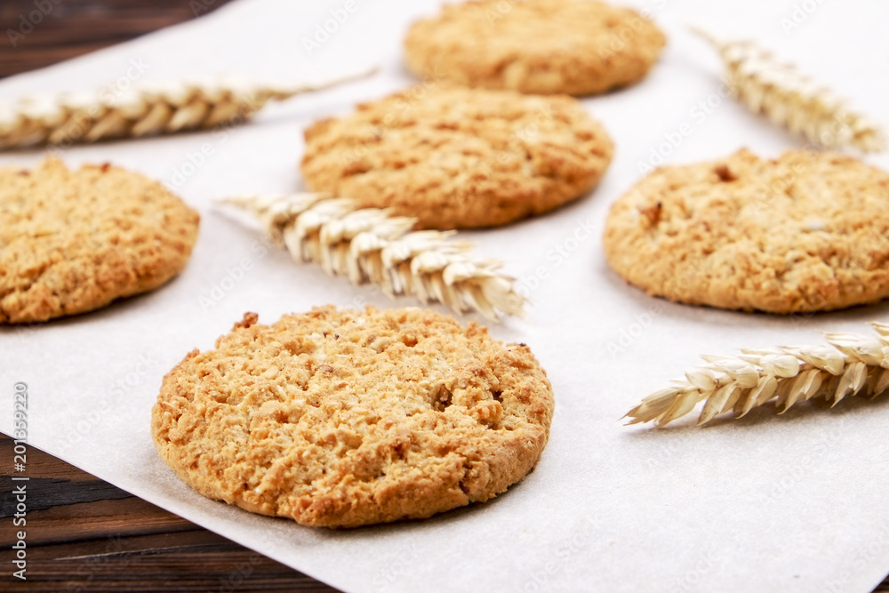 Healthy vegan integral cookies made of hazelnut powder on baking paper, dark brown wooden table background. Home made vegetarian gluten free snack w/ nuts. Decorative wheat spica. Close up, copy space Healthy vegan integral cookies made of hazelnut powder on baking paper, dark brown wooden table background. Home made vegetarian gluten free snack w/ nuts. Decorative wheat spica. Close up, copy space