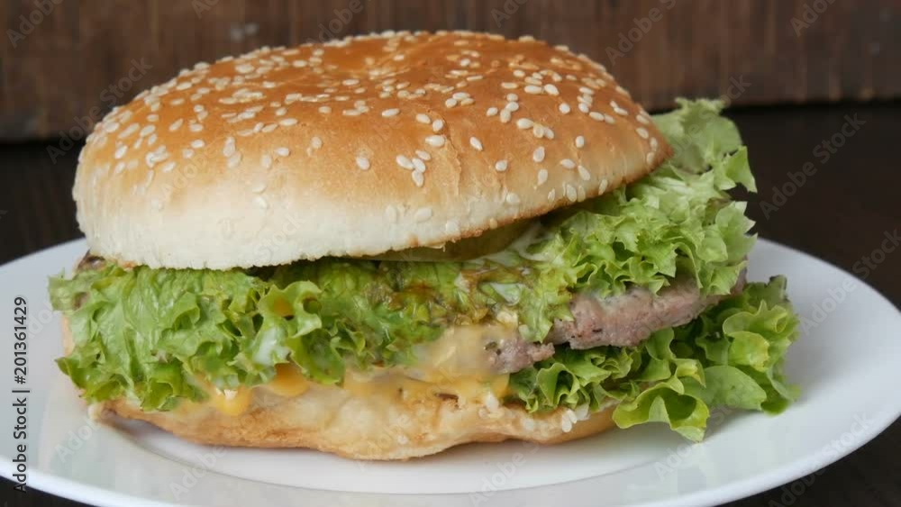 Large triple burger with lettuce leaves on a white plate. Hamburger on a stylish wooden background. Fast food Large triple burger with lettuce leaves on a white plate. Hamburger on a stylish wooden background. Fast food