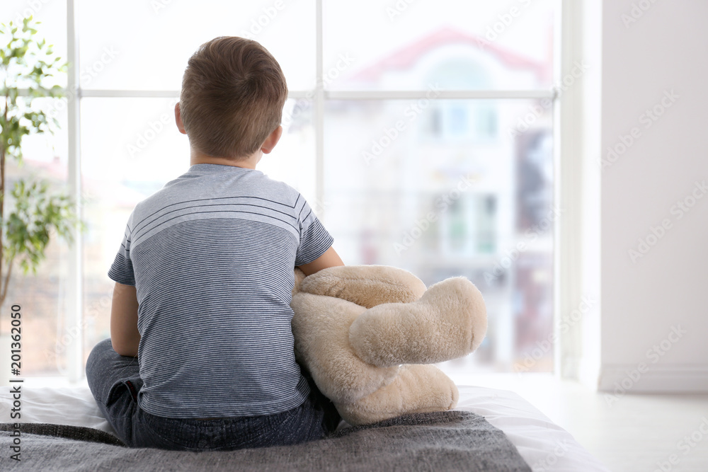 Lonely little boy sitting on bed in room. Autism concept Lonely little boy sitting on bed in room. Autism concept