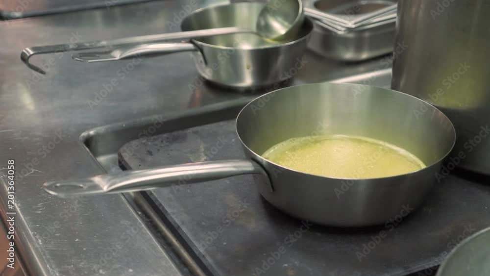 Melt butter on high heat for cooking dishes or roasting. Kitchen of restaurant or cafe or catering. Metal cabinets and tables, working atmosphere in the kitchen. Stainless steel cookware on the table Melt butter on high heat for cooking dishes or roasting. Kitchen of restaurant or cafe or catering. Metal cabinets and tables, working atmosphere in the kitchen. Stainless steel cookware on the table