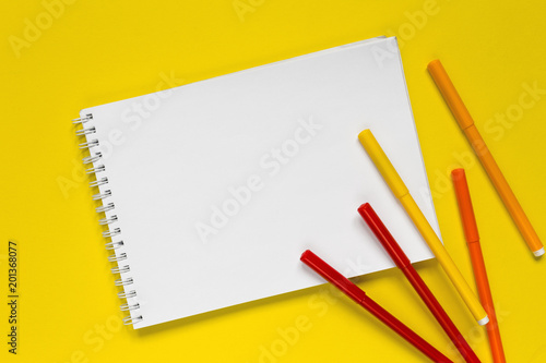 Multicolored markers on a white notepad on a yellow background flat lay top view with copy space,layout,mocap