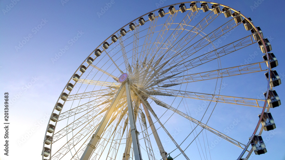 Majestic observation wheel rotating in amusement park, sunny blue sky background