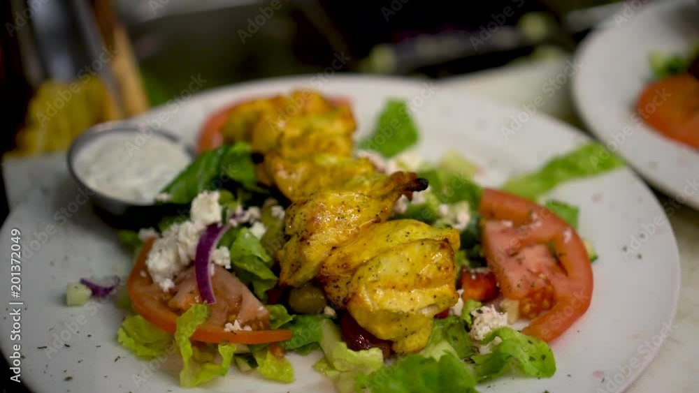 Beautiful Mediterranean salad and a cook slides chicken pieces off of a skewer onto the salad. Beautiful Mediterranean salad and a cook slides chicken pieces off of a skewer onto the salad.