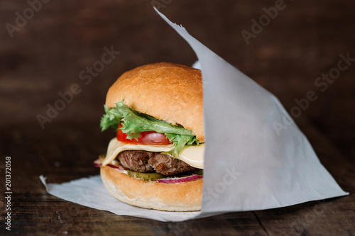 fresh tasty burger wrapped on white paper on wooden table. With empty place for title
