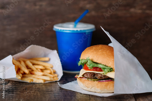 fresh tasty burger wrapped on white paper on wooden table. With empty place for title
