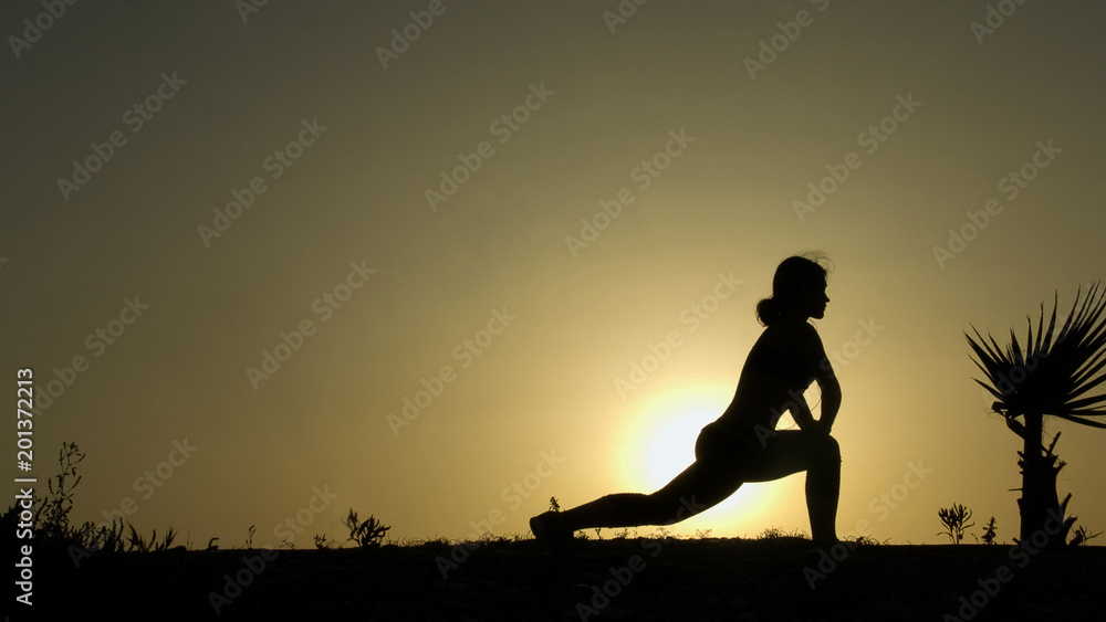 Silhouette of concentrated girl performing yoga poses, meditating against sunset