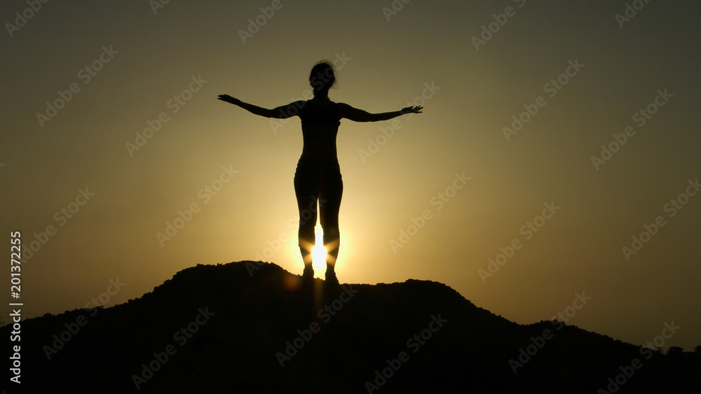 Silhouette on top of hill greeting sunrise with raised hands, aspiration, hope
