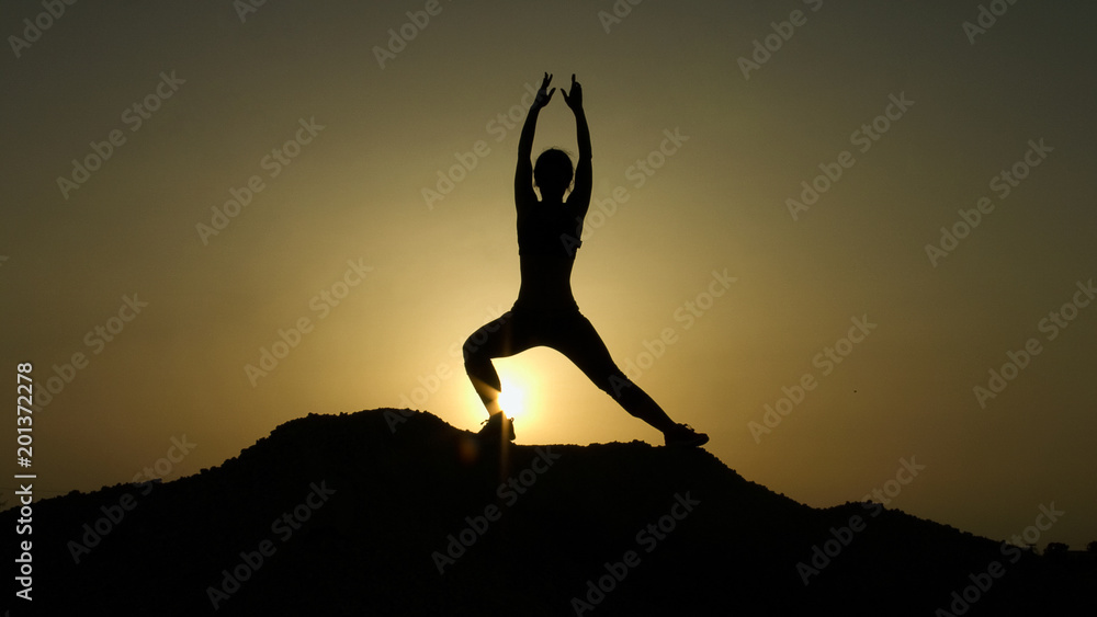 Silhouette of young woman enjoying harmony with nature while practicing yoga