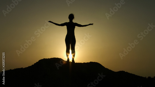 Silhouette on top of hill greeting sunrise with raised hands, aspiration, hope
