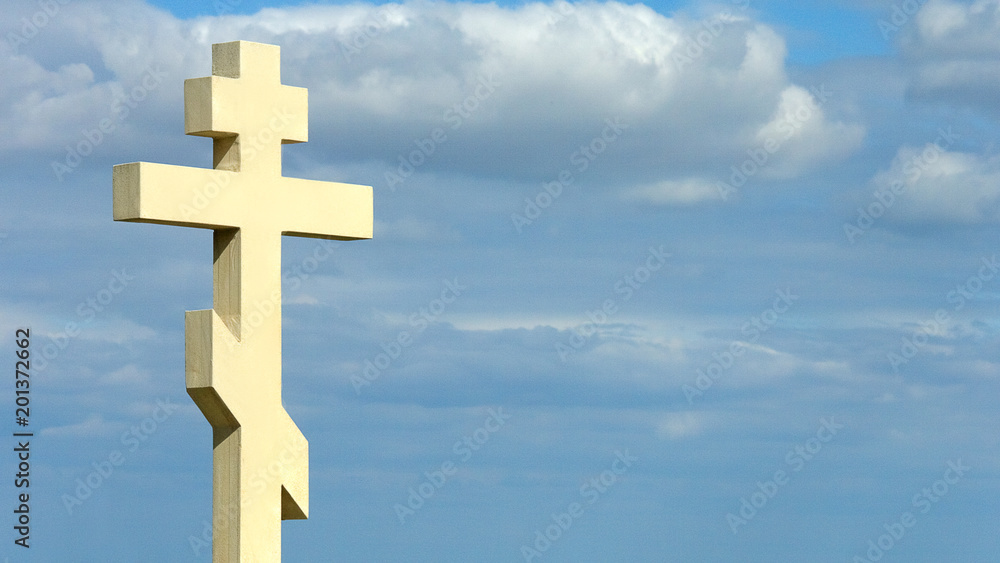 Stone cross on blue cloudy sky background, strong spiritual faith, christianity Stone cross on blue cloudy sky background, strong spiritual faith, christianity