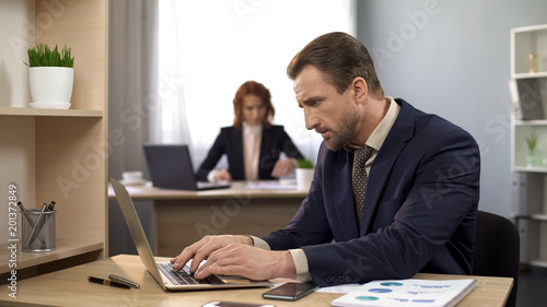 Office manager typing data on laptop, finishing project, satisfied with results