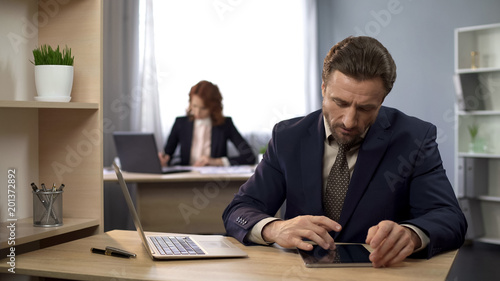 Company worker typing on laptop, searching information on tablet, analysis