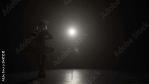 Beautiful teenage ballerina girl dreaming of a ballet career while rehearsing graceful moves in a dark studio in slow motion
