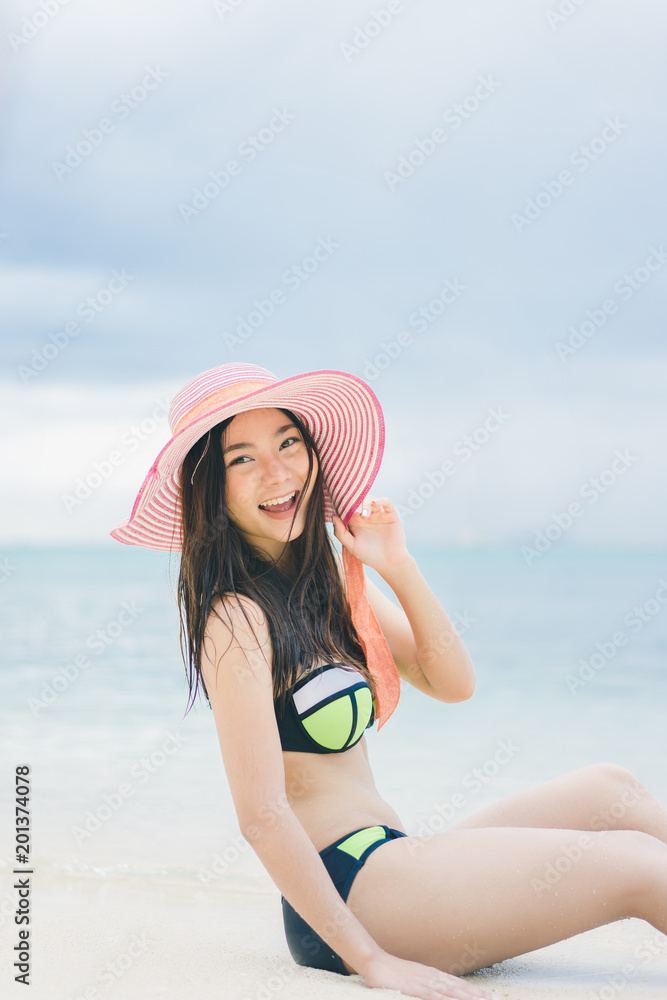 Pretty beautiful asian woman wearing blue swimwear bikini with hat living sunbathing on the beach in the summer