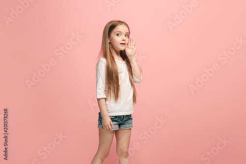 The young teen girl whispering a secret behind her hand over pink background