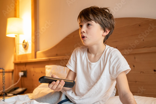 Child on the bed watching TV holding the remote control