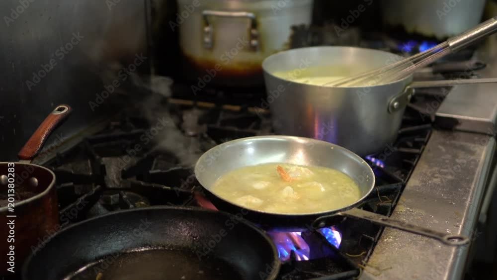 Chef pouring oil into a pan with shrimp and butter in it on a fire in a kitchen. Chef pouring oil into a pan with shrimp and butter in it on a fire in a kitchen.