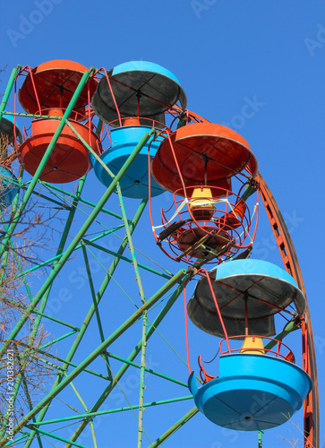 Closeup of the empty cars of the stopped Ferris wheel amusement ride with the damaged cabin in the middle against a blue sky