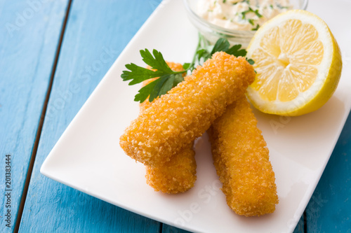 crispy fried fish fingers with lemon and sauce on blue wooden background