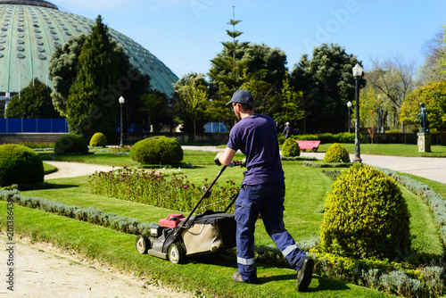 Worker cutting the grass of a municipal park. Worker using a gasoline machine to mow the lawn of a park.