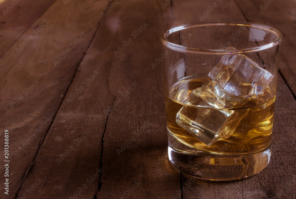 Whiskey in glass with ice cubes on wooden table Whiskey in glass with ice cubes on wooden table