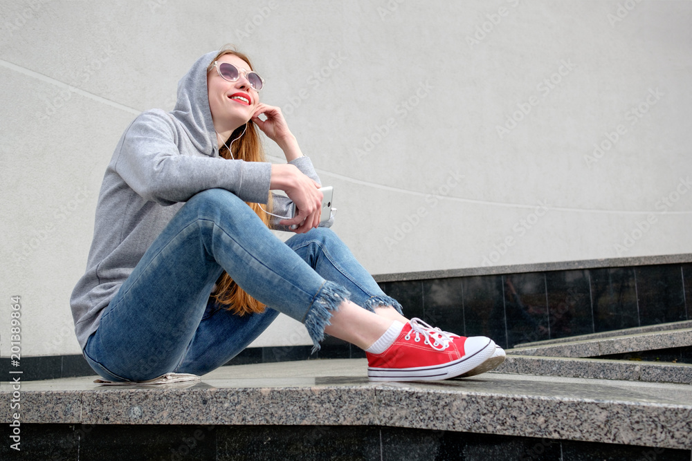 Redhead girl dressed in hoody, jeans and red sneakers Redhead girl dressed in hoody, jeans and red sneakers