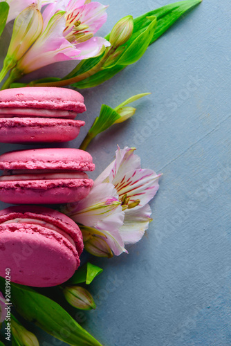 Fototapeta Naklejka Na Ścianę i Meble -  Pink macaroon close-up with spring flowers and buds. French dessert on a blue stone background with copy space.