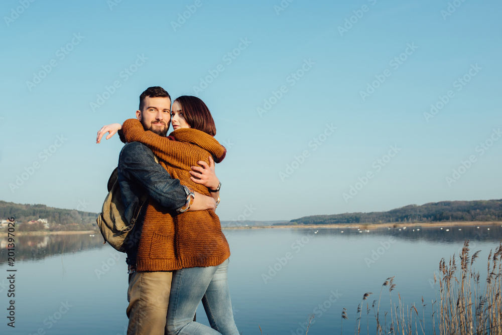 Travel and love. Happy young couple walking along the shore of blue lake in hipster clothes