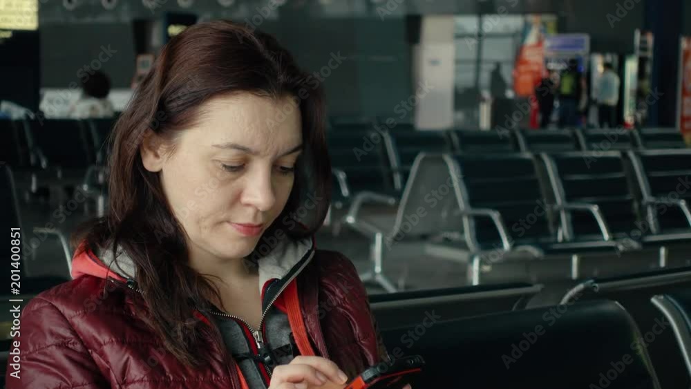A woman with a phone in her hands. She is sitting while waiting for the flight. A woman with a phone in her hands. She is sitting while waiting for the flight.