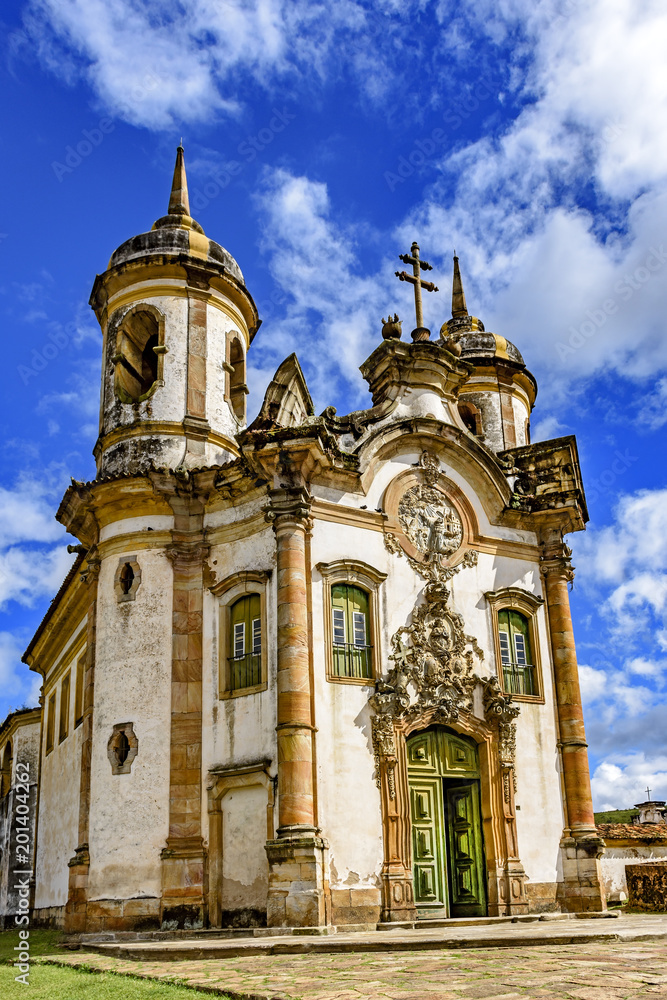Fototapeta premium Facade of the church of São Francisco de Paula in Ouro Preto, Minas Gerais with its windows, large wooden door, stone arch, towers, and baroque sculptures