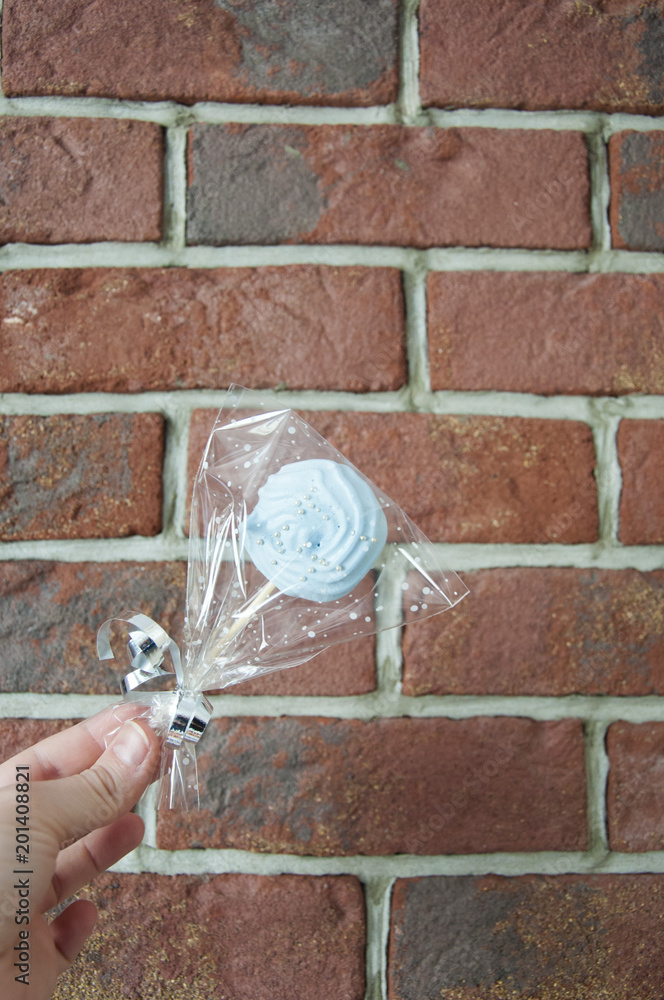 Obraz Wrapped candy with transparent cellophane in female hand on brick wall background, copy space.