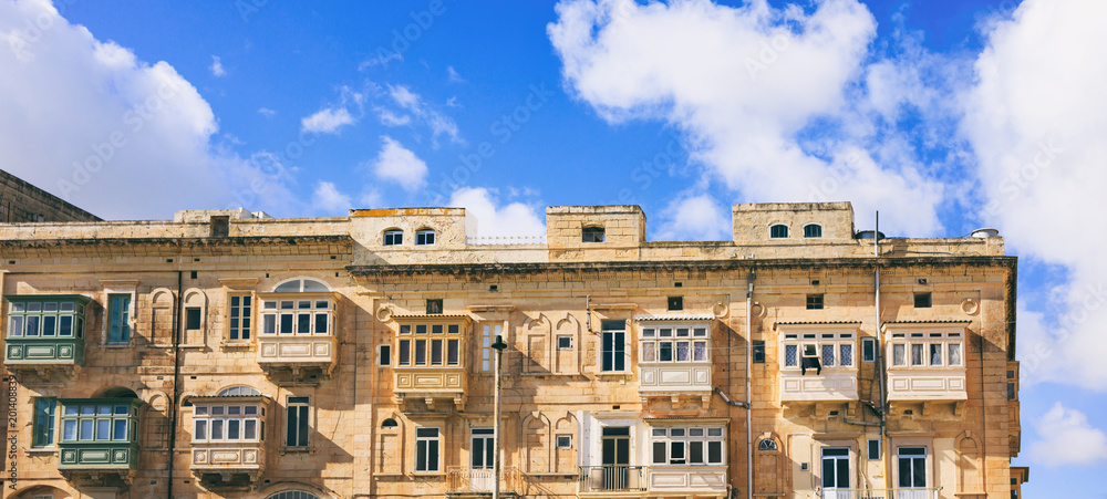 Malta, Valletta, building facade with covered balconies, with blue sky background, front view