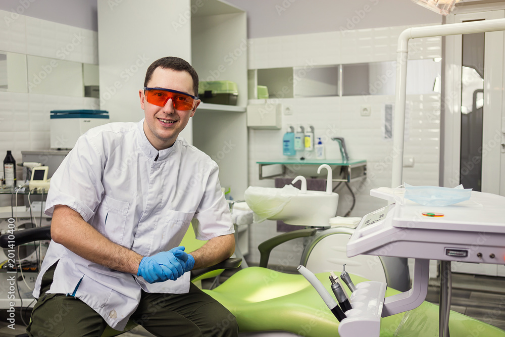Male dentist standing over medical office background. Healthcare, profession, stomatology and medicine concept Male dentist standing over medical office background. Healthcare, profession, stomatology and medicine concept