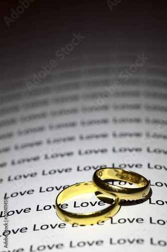 Two gold wedding rings on a page with the word love repeated