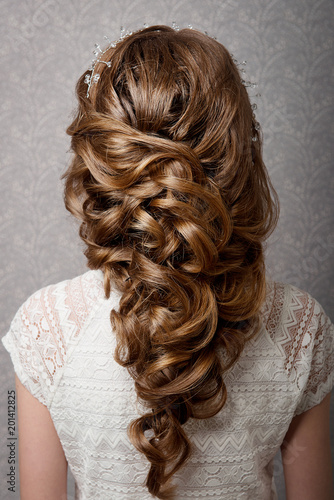 A greek braid on the head of a brown-haired woman rear view on a gray background. Professional female hairdress.