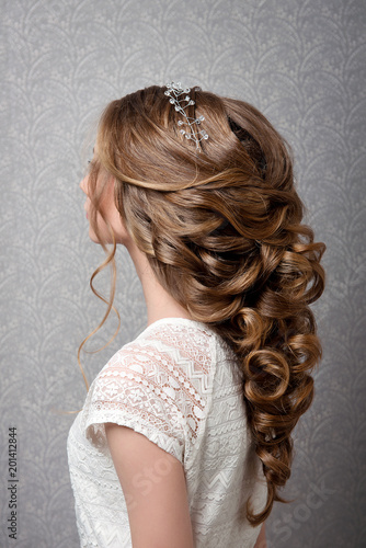 Wedding hairstyle on the head of a brown-haired woman view in profile on a gray background. Professional female hairdress.