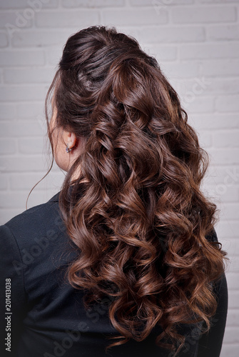 Hairstyle long curls on the head of the brunette left view on the background of a white brick wall close-up.Professional women's hairstyle.