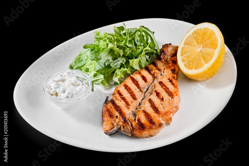 plate with grilled salmon with lemon and greens on a black background.