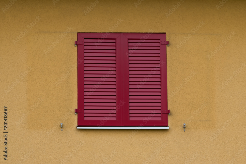 Red wooden shutters on a building with yellow painted walls.