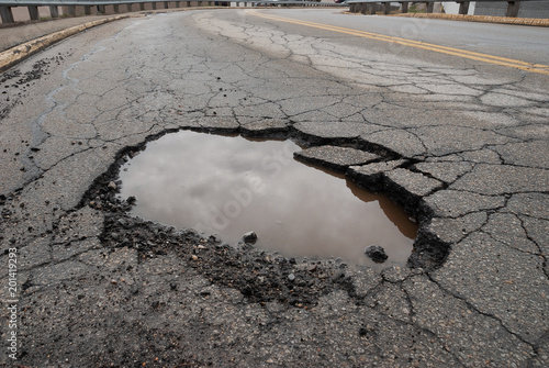 Pothole in road with broken asphalt after spring thaw photo