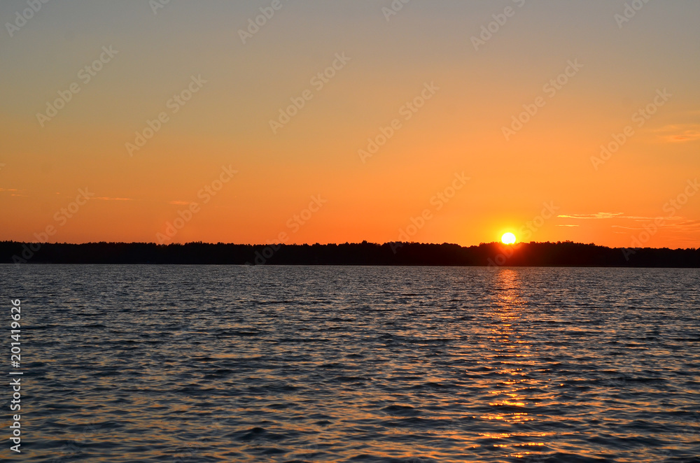 Beautiful orange sunset over the lake with setting sun reflected in the water