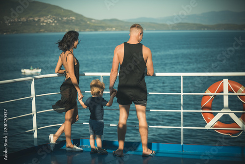 Family travelling on cruise ship on sunny day. Family with cute son on summer vacation. Father, mother and child stand on deck of cruise liner with sea waves on background. Family rest concept. © Volodymyr