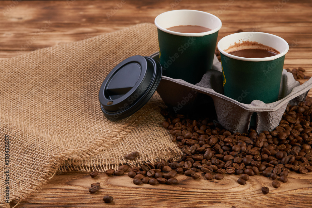Close-up of three take away green paper cups in coffee holder container  with coffee beans and hot chocolate drink on rustic wooden table  background, top view, Stock Photo