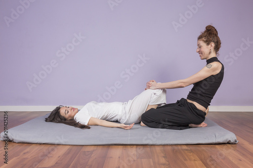Young woman lying while enjoying stretching and the acupressure techniques of traditional Thai massage on her legs and feet at spa and wellness center