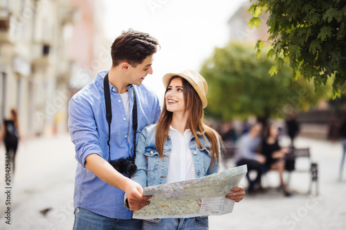 Young Couple of tourists is exploring new city together. Smiling and look at the map on the city street